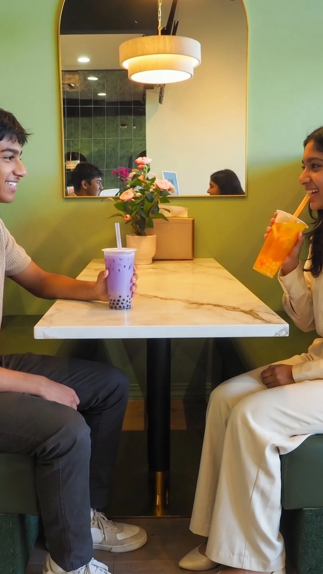 A couple sitting across from each other in a booth, enjoying boba drinks.