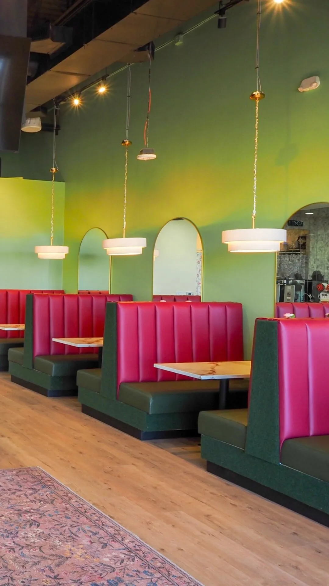Open dining area at Badger & Bloom Boba showing pink booths, pendant lighting, and fresh flowers by the counter.